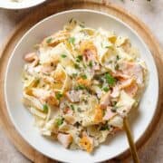 Pappardelle with roasted salmon, creamy white sauce, black pepper, and fresh herbs on a white plate.