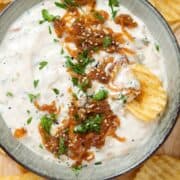 Onion dip garnished with caramelized onions in a stripped green bowl with crinkle cut chips all around the bowl.