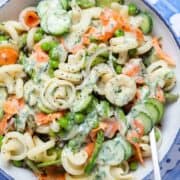 Creamy pasta salad with smoked salmon, peas, and asparagus in a white bowl on a blue tile background.