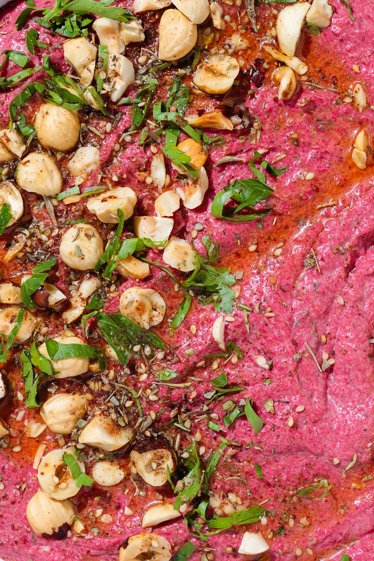 Bright pink beet dip in a white bowl with a blue rim garnished with hazelnuts, parsley, and olive oil.