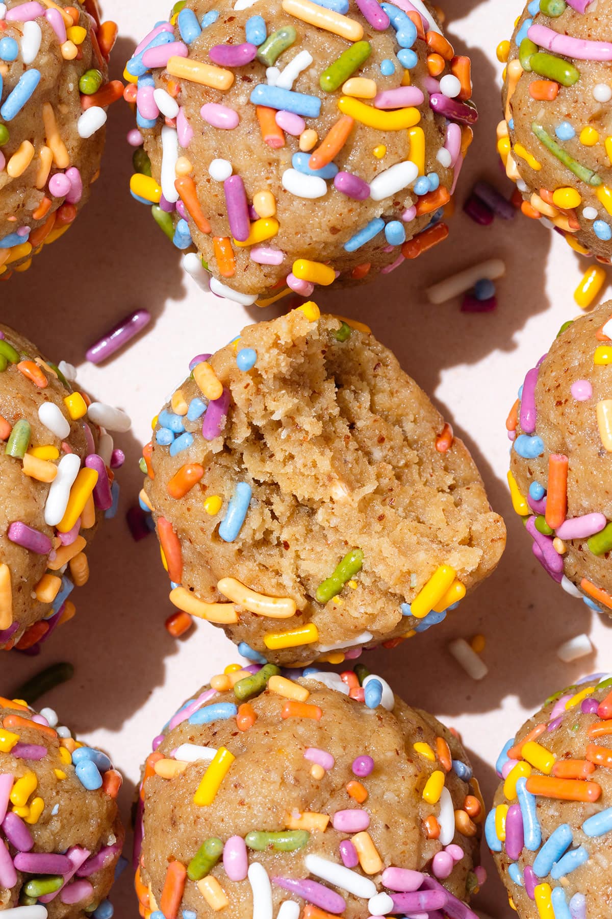 Protein balls covered with multi-colored sprinkles evenly laid out on a light pink plate.