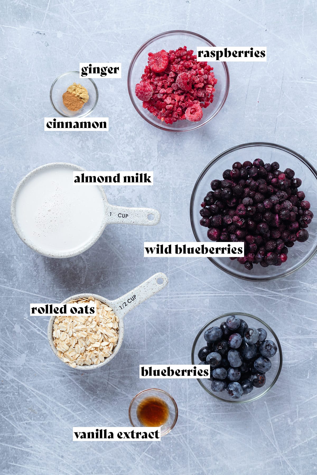Ingredients for blueberry oatmeal laid out on a grey background.