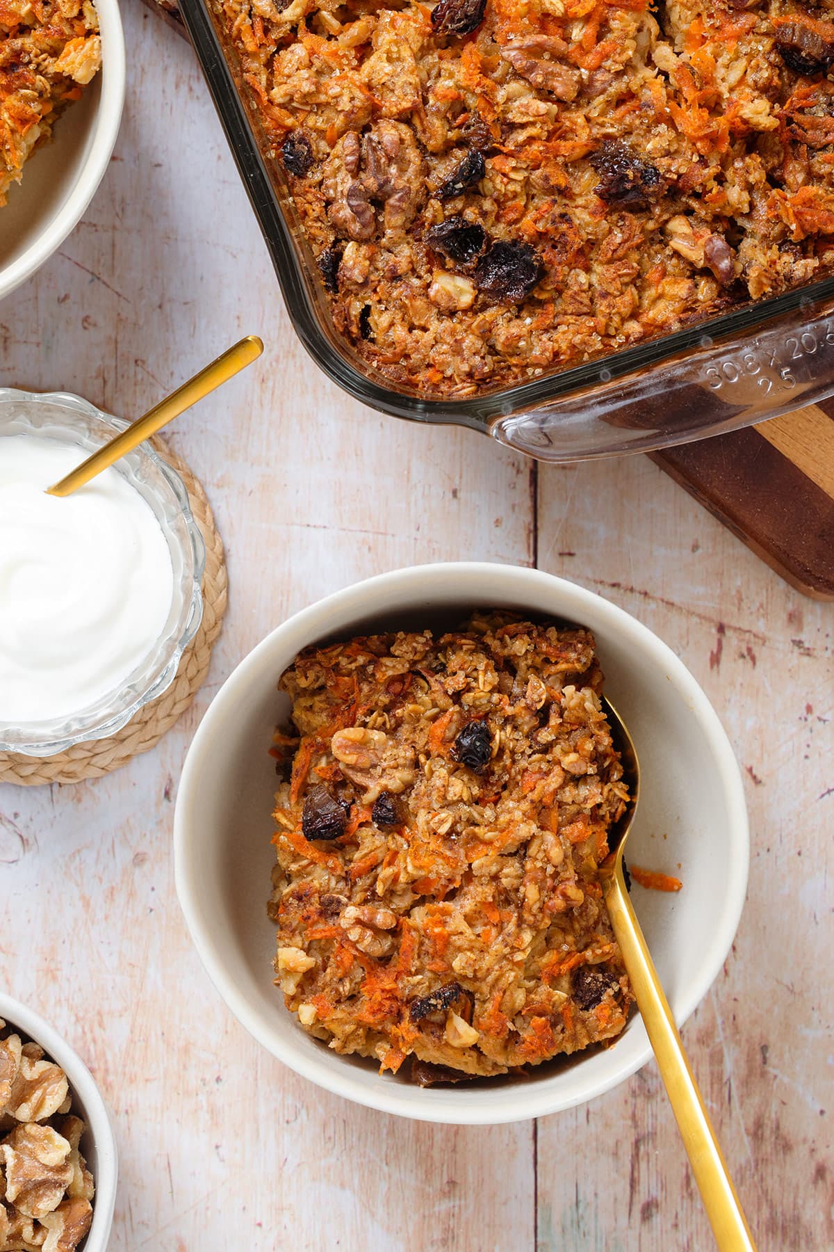 A slice of carrot cake baked oatmeal in a white bowl with a gold spoon on a wooden background.
