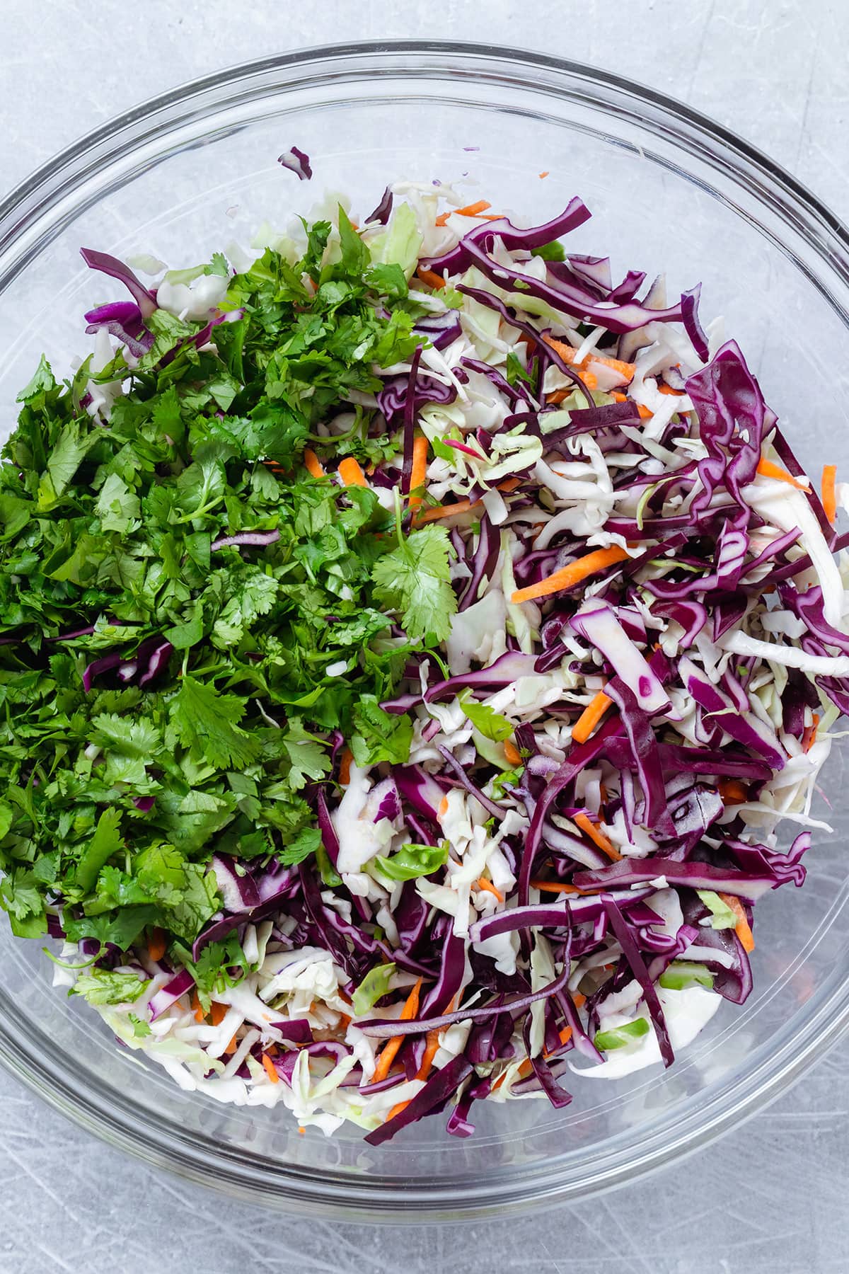 Colorful coleslaw mix and chopped fresh cilantro in a large glass bowl.