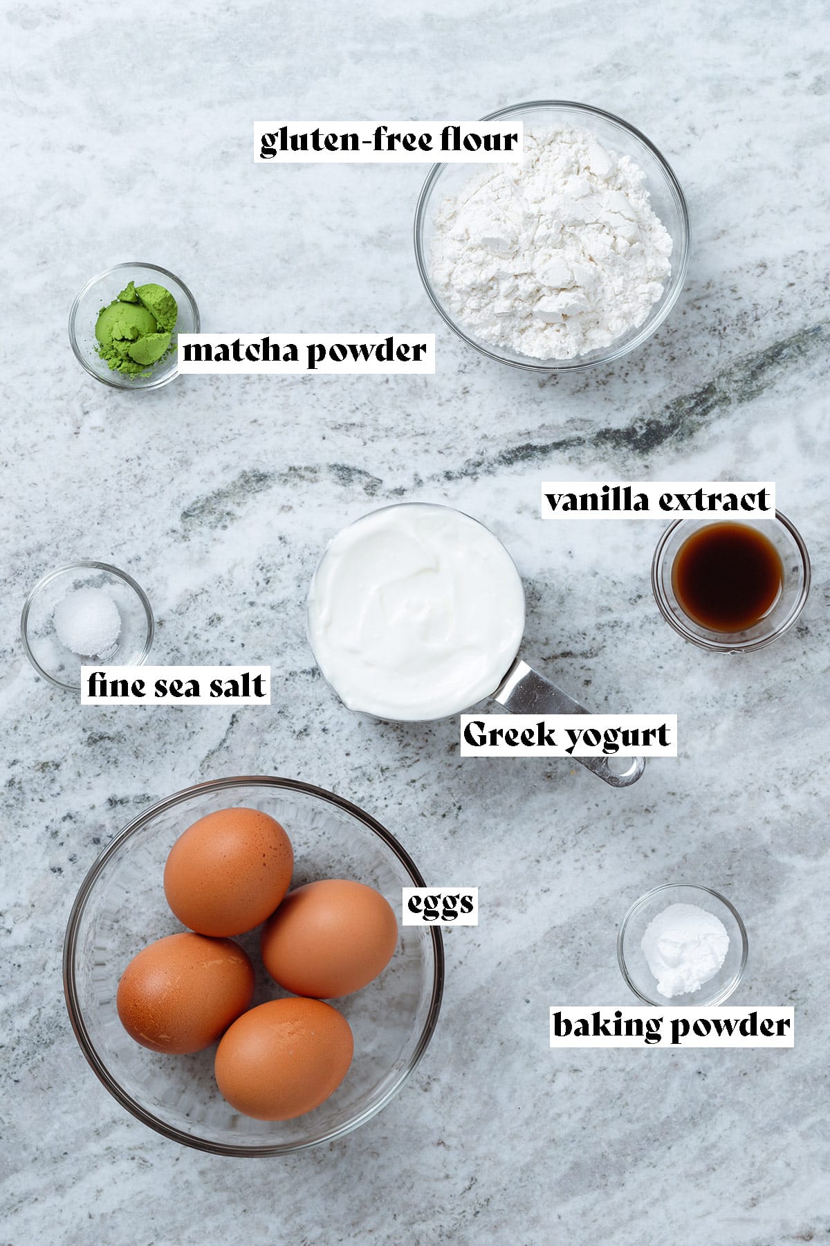 Eggs, flour, Greek yogurt, matcha powder, and other ingredients laid out on a stone background with text overlay.