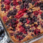 Baked oatmeal with mixed berries in a large glass baking dish on a wooden cutting board.