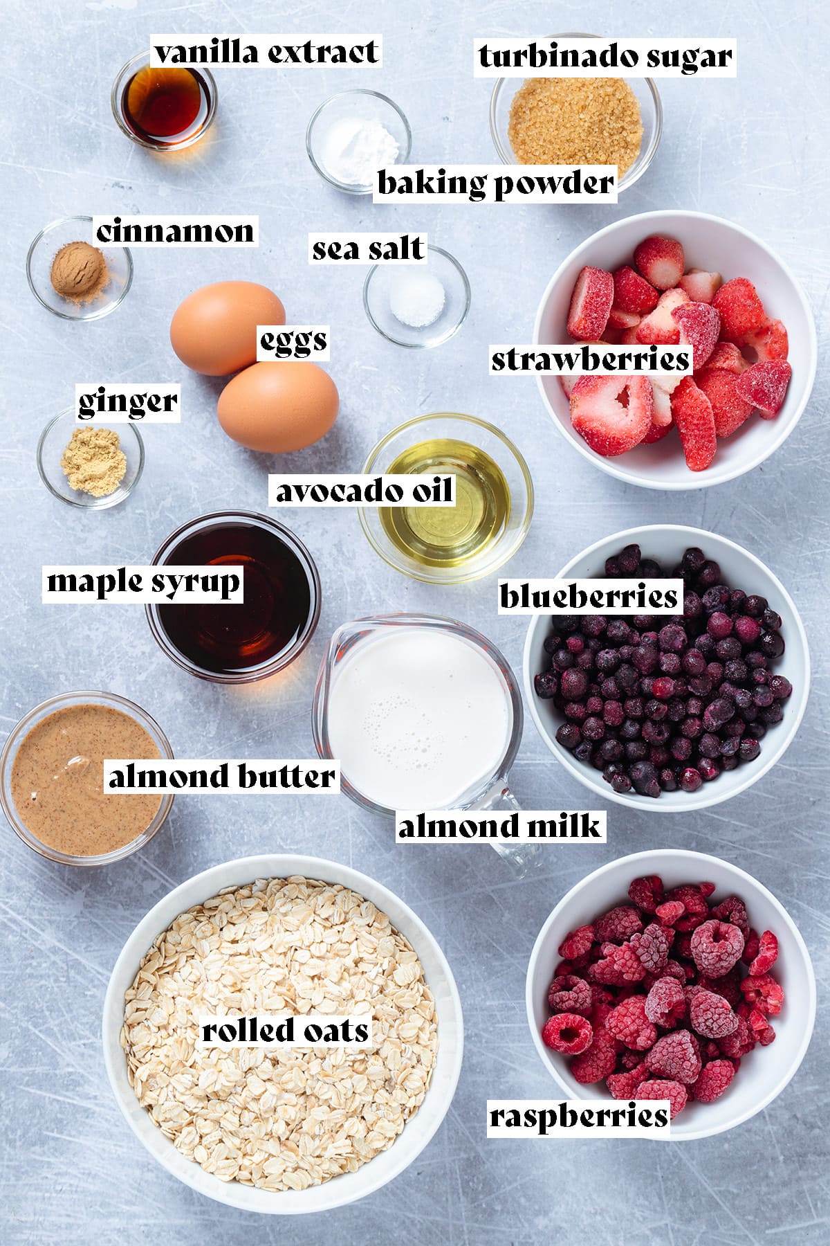 Ingredients for baked oatmeal like oats, berries, milk, oil, and eggs laid out on a grey background.