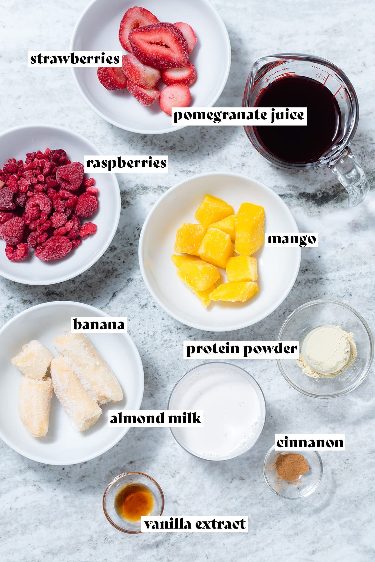 Ingredients like frozen mango, berries, almond milk, and protein powder on a stone background.
