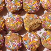 Protein balls covered with multi-colored sprinkles evenly laid out on a light pink plate.