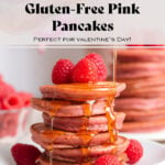 A stack of pink pancakes on a small white plate garnished with fresh raspberries and being drizzled with maple syrup.