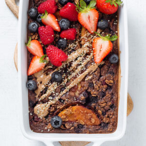 Baked oatmeal in a white baking dish garnished with fresh berries and almond butter and hemp seeds.