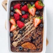 Baked oatmeal in a white baking dish garnished with fresh berries and almond butter.