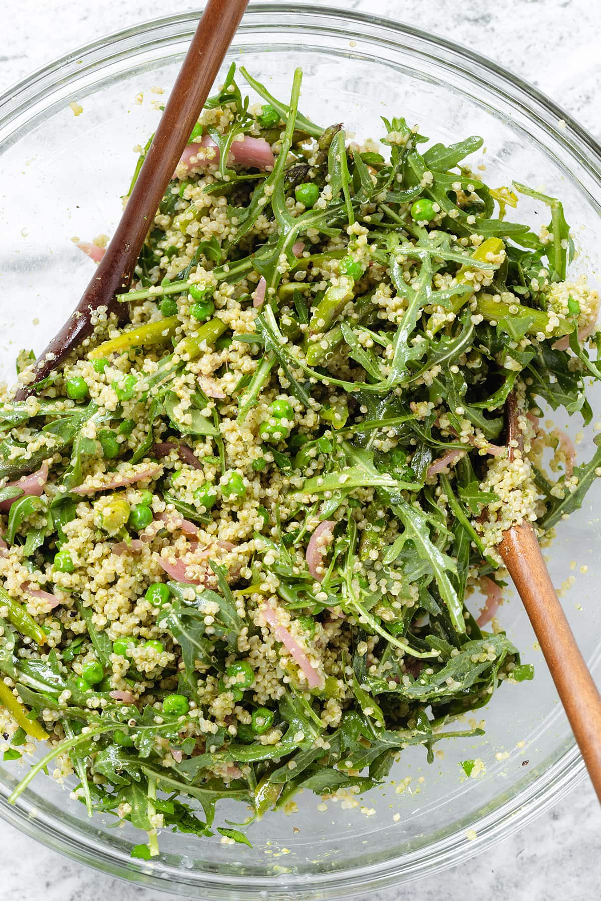 Asparagus quinoa salad in a large glass bowl with wooden mixing spoons.