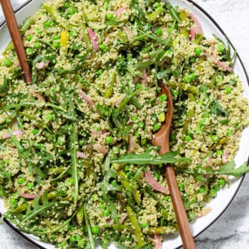 Quinoa salad with arugula, asparagus, and peas on a large serving platter with wooden spoons inserted in it.