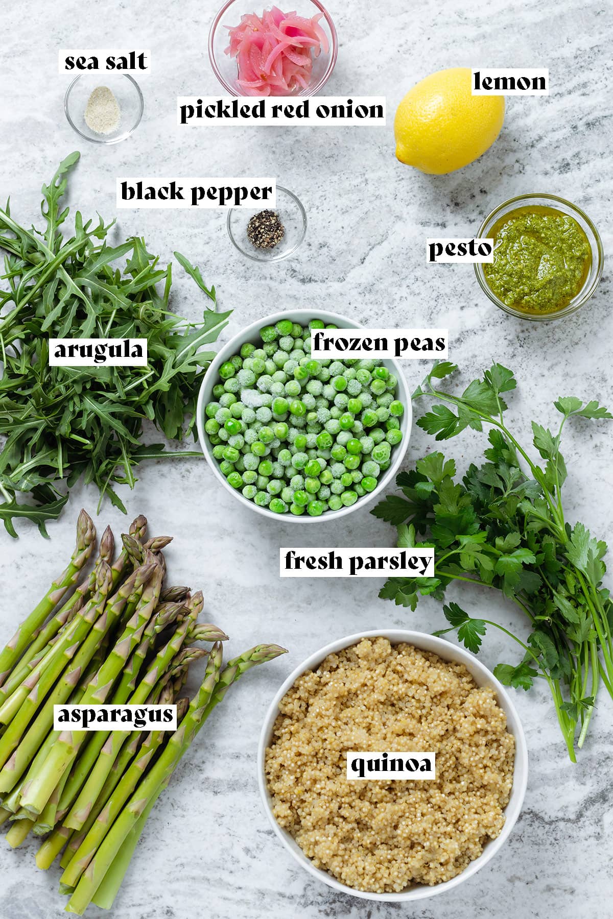Asparagus, arugula, frozen peas, quinoa, and other ingredients laid out on a stone background.