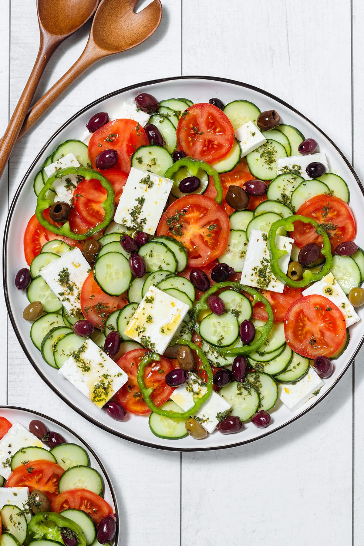 Layered Greek Salad on a large white platter with light herb vinaigrette drizzled over it.