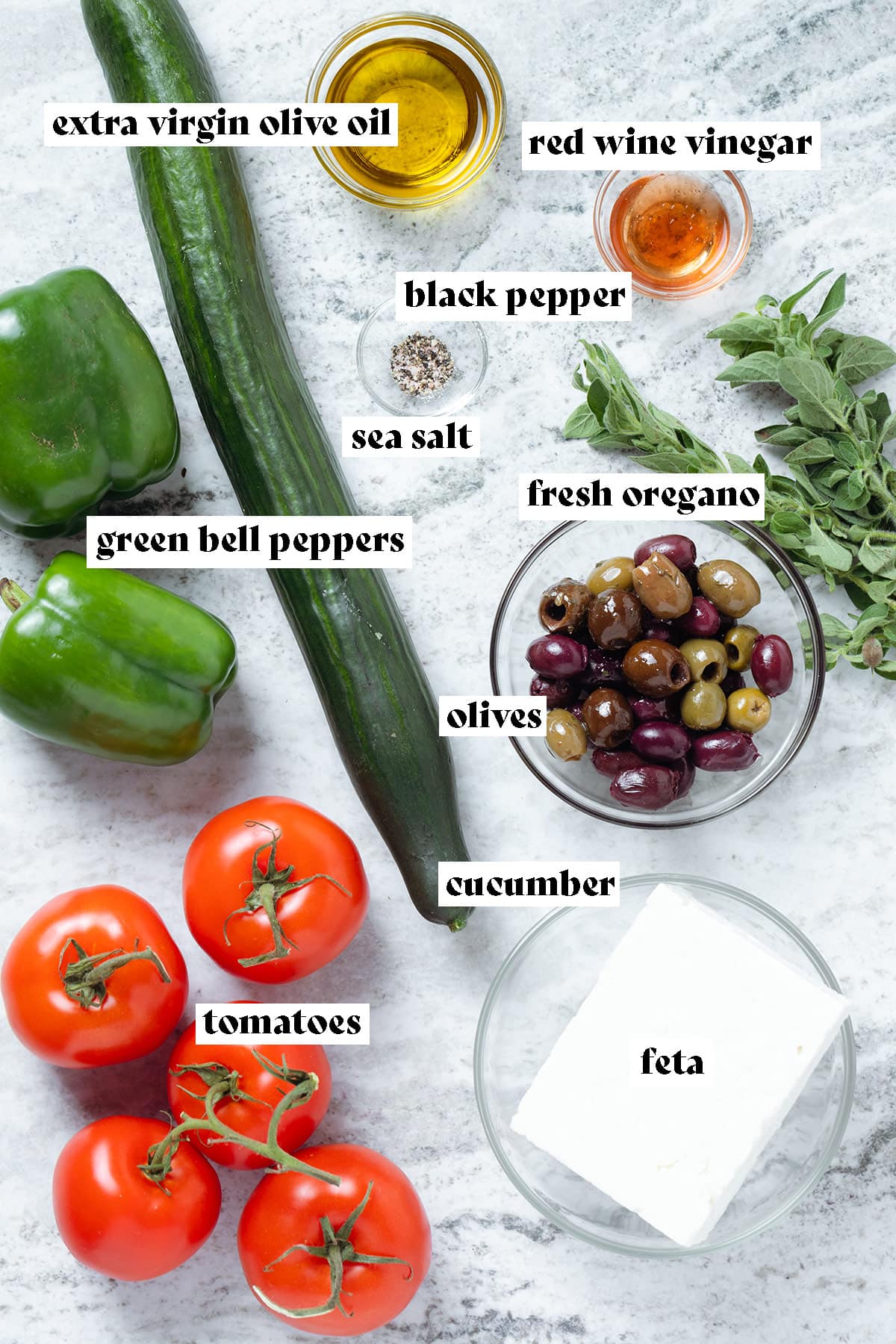 Ingredients for like cucumber, tomatoes, bell peppers, olives, and feta on a stone bagkround.