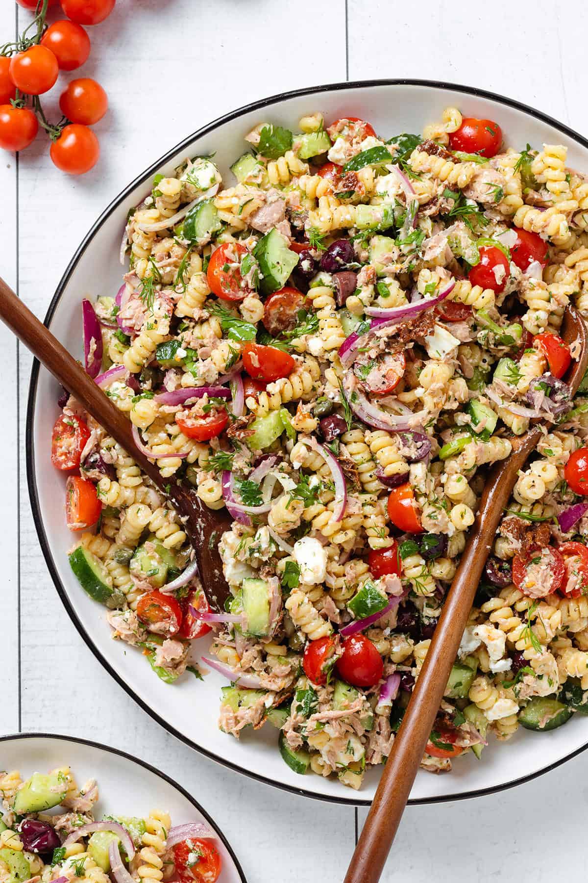 Tuna pasta salad on a large white serving plate with a black rim and two wooden serving spoons inserted in.