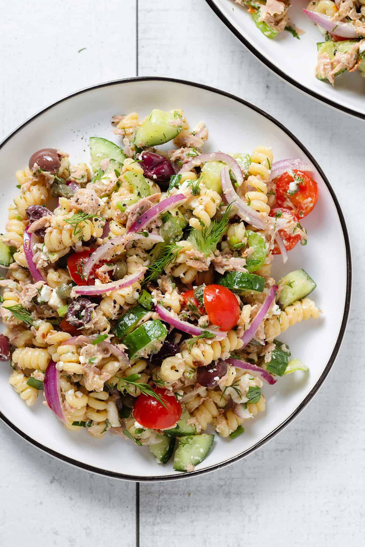 Tuna pasta salad on a white plate with a black rim and two wooden serving spoons inserted in.