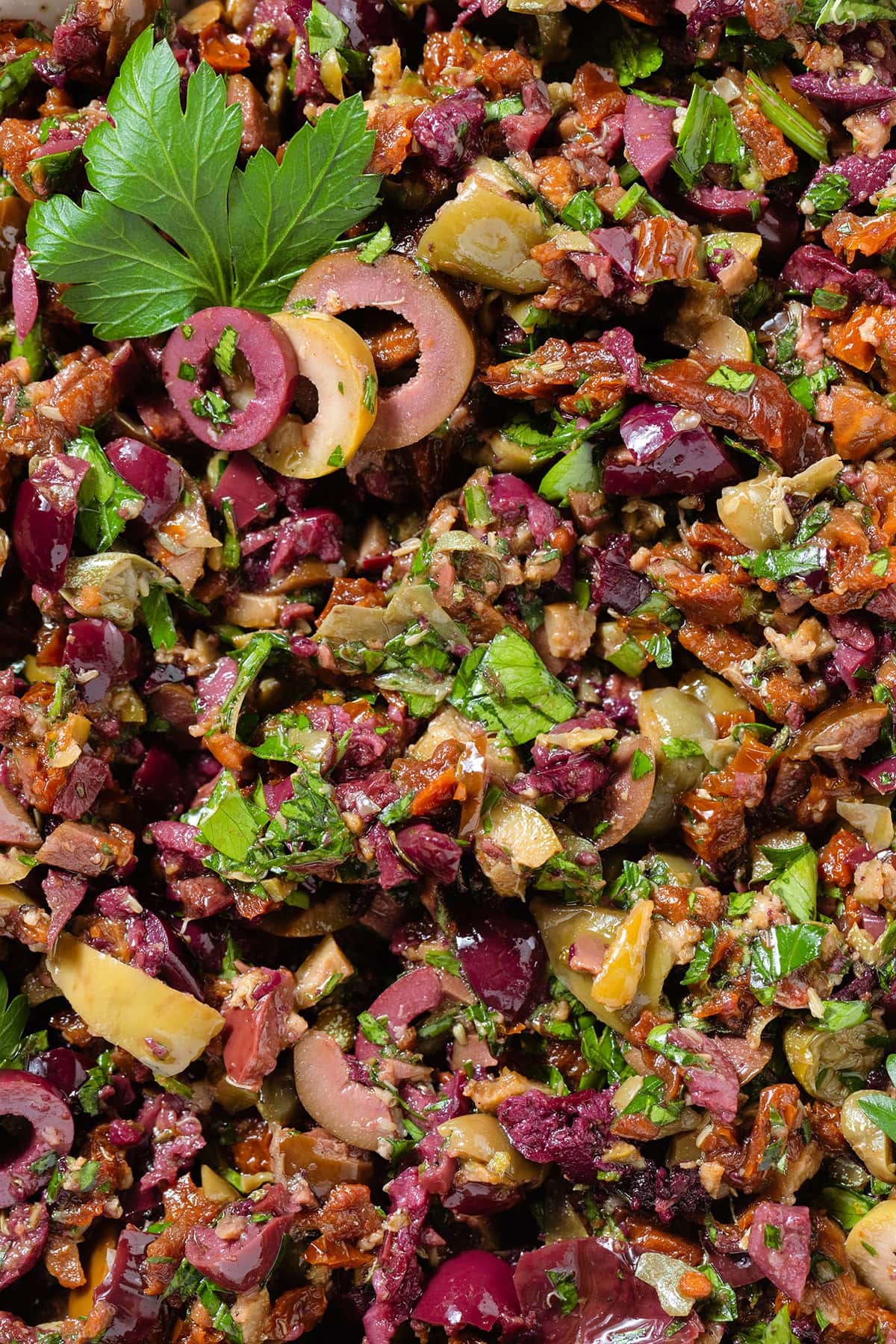 Olive tapenade with sundried tomatoes garnished with fresh parsley and olive slices.