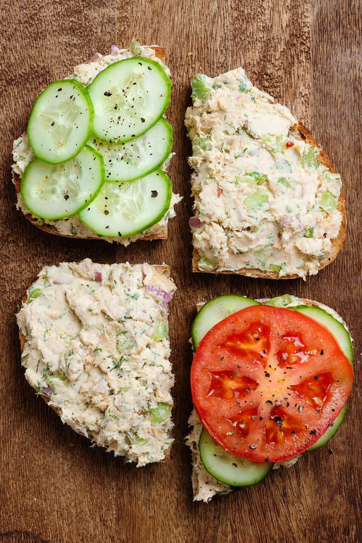 Slices of sourdough bread on a wooden cutting board topped with salmon spread, tomatoes, and cucumber.