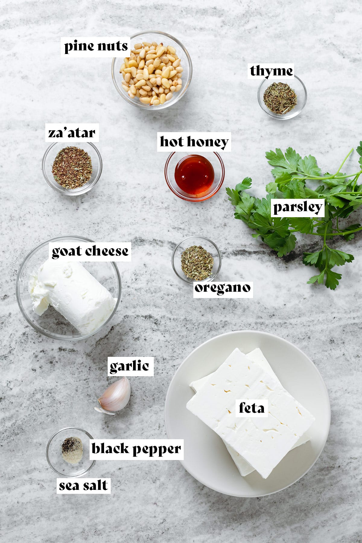 Feta, goat cheese, hot honey, and other ingredients for a dip laid out on a stone background.