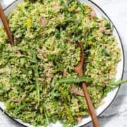 Quinoa salad with arugula, asparagus, and peas on a large serving platter with wooden spoons inserted in it.
