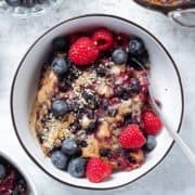 A slice of blueberry baked oatmeal in a white bowl with black rim garnished with berries and almond butter.