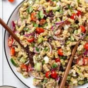 Tuna pasta salad on a large white serving plate with a black rim and two wooden serving spoons inserted in.