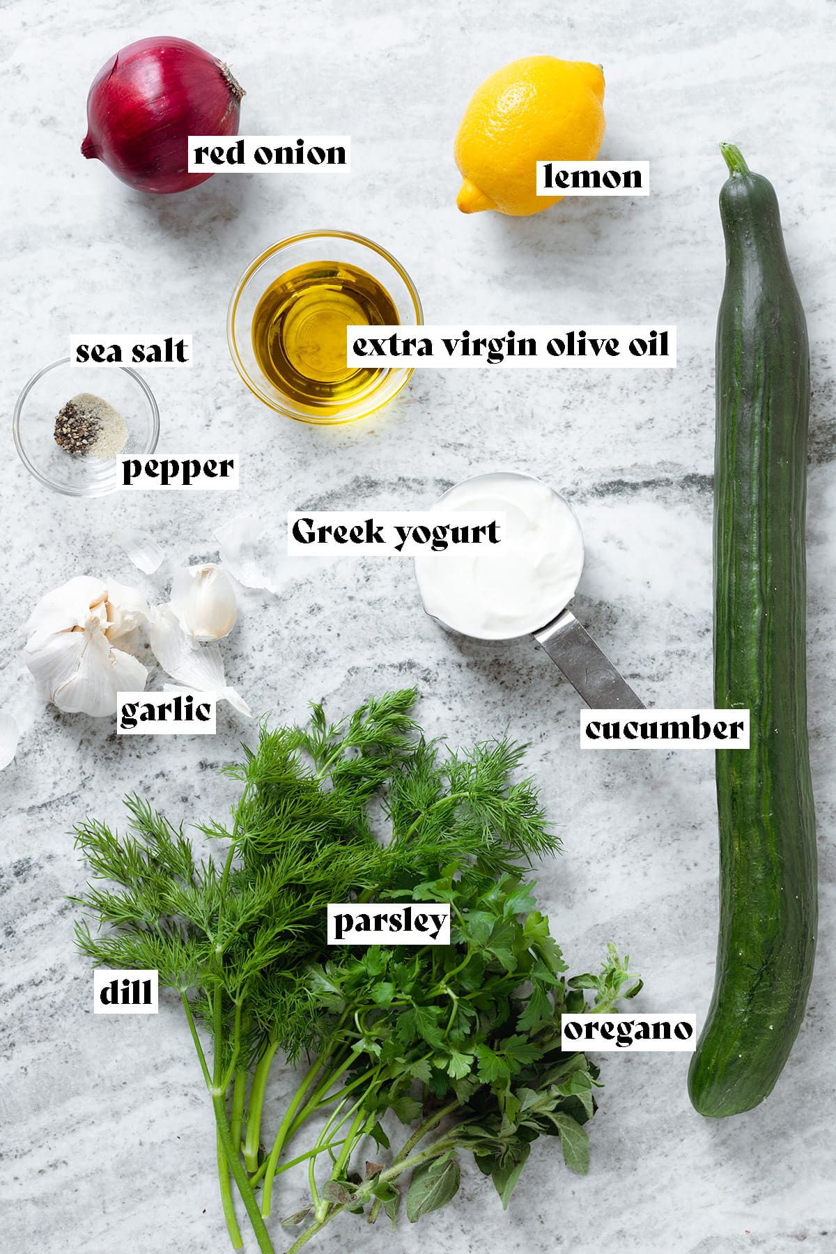 Ingredients like cucumber, fresh herbs, and lemon laid out on a white stone backdrop.