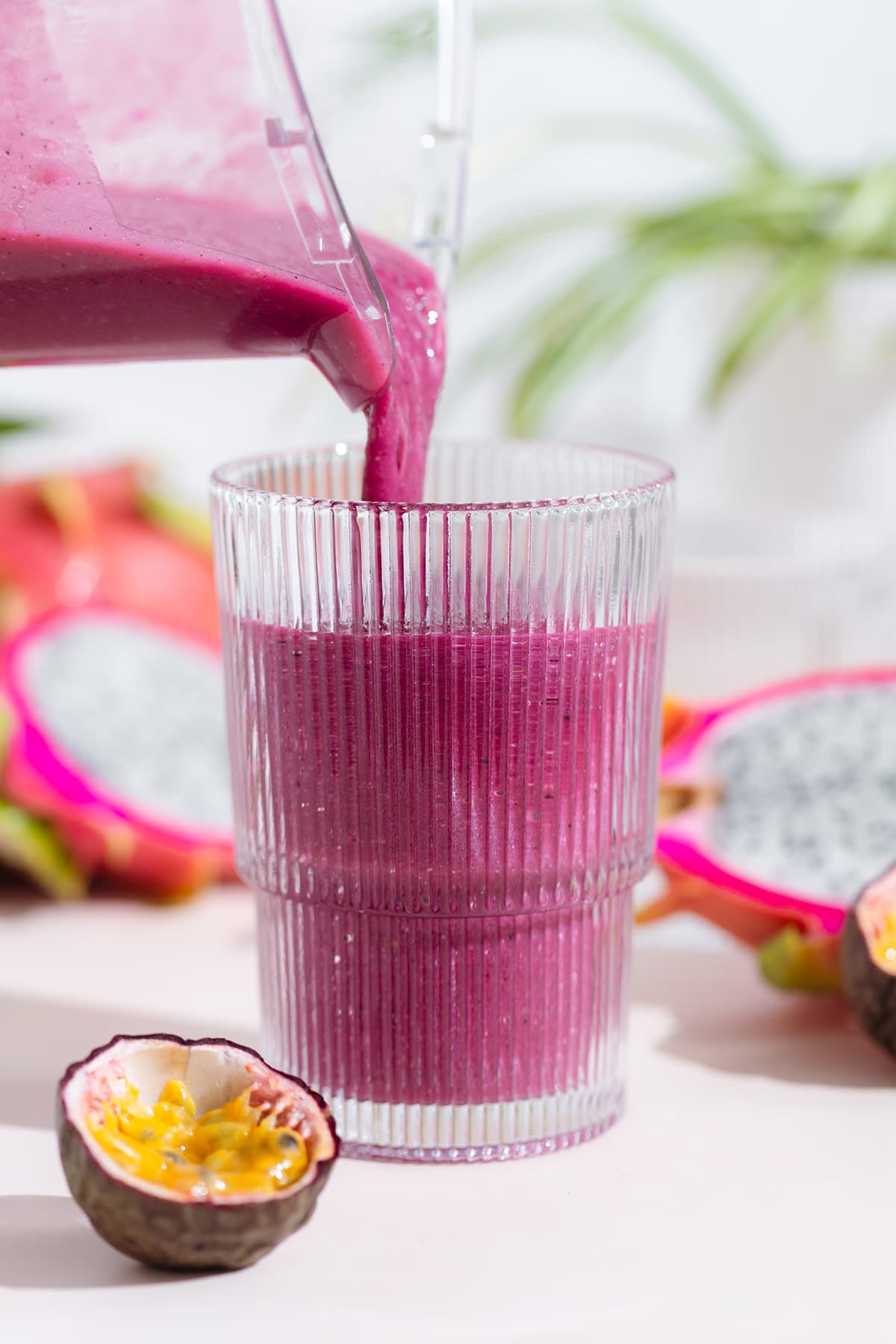 Bright purple dragon fruit garnished being poured into a tall glass from a high-speed blender.