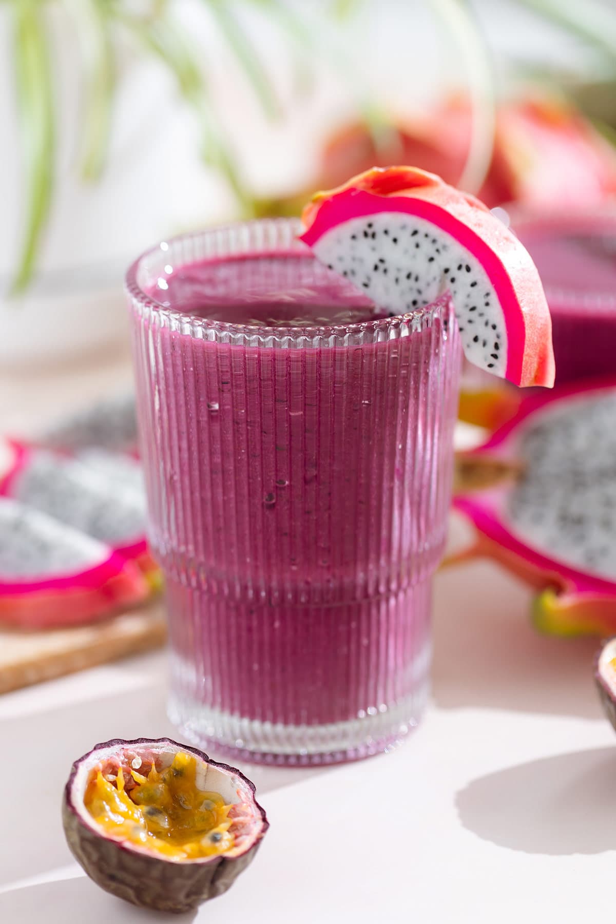 Bright purple smoothie in a tall glass garnished with white dragon fruit with more dragon fruit and passion fruit around the glass.