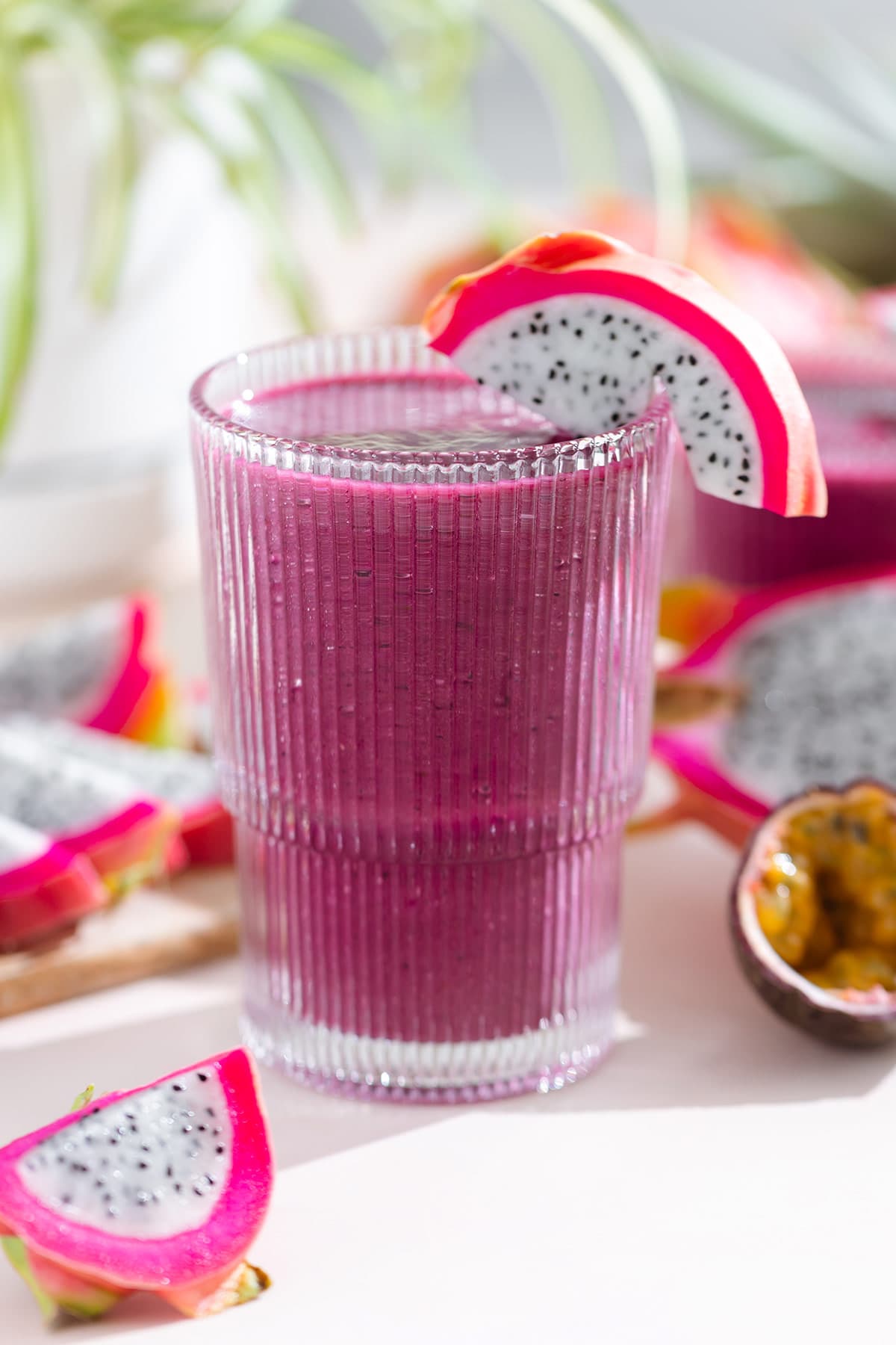 Bright purple smoothie in a tall glass garnished with white dragon fruit with more dragon fruit and passion fruit around the glass.
