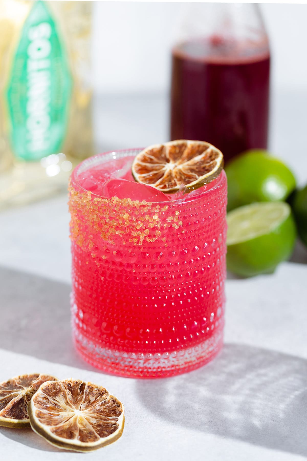 Bright pink margarita in a short glass garnished with a dehydrated lime slice on a white background.
