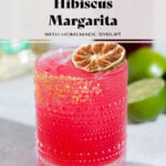Bright pink margarita in a short glass garnished with a dehydrated lime slice on a white background.