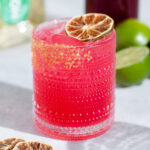 Bright pink margarita in a short glass garnished with a dehydrated lime slice.