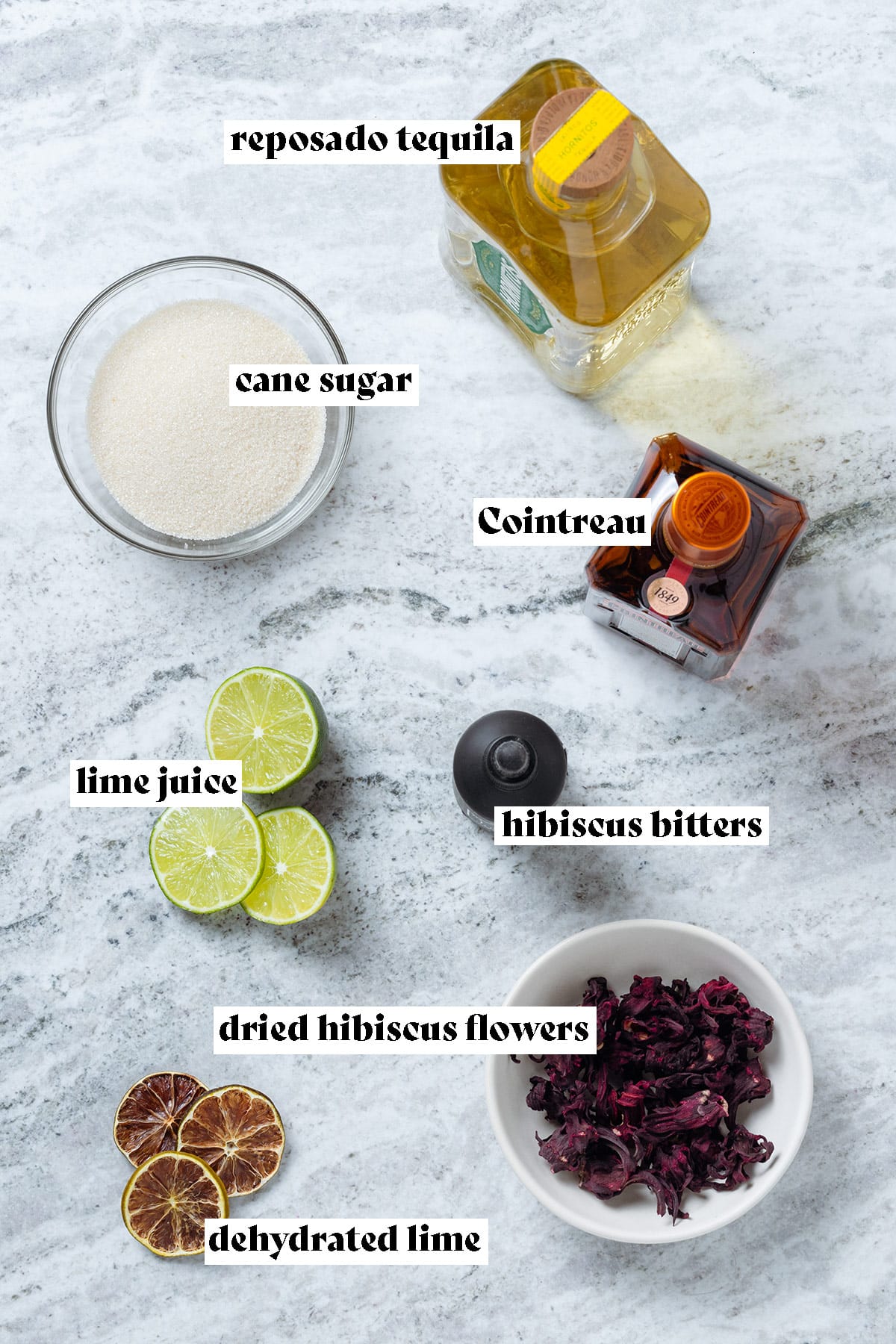 Ingredients for a hibiscus margarita laid out on a grey stone background.