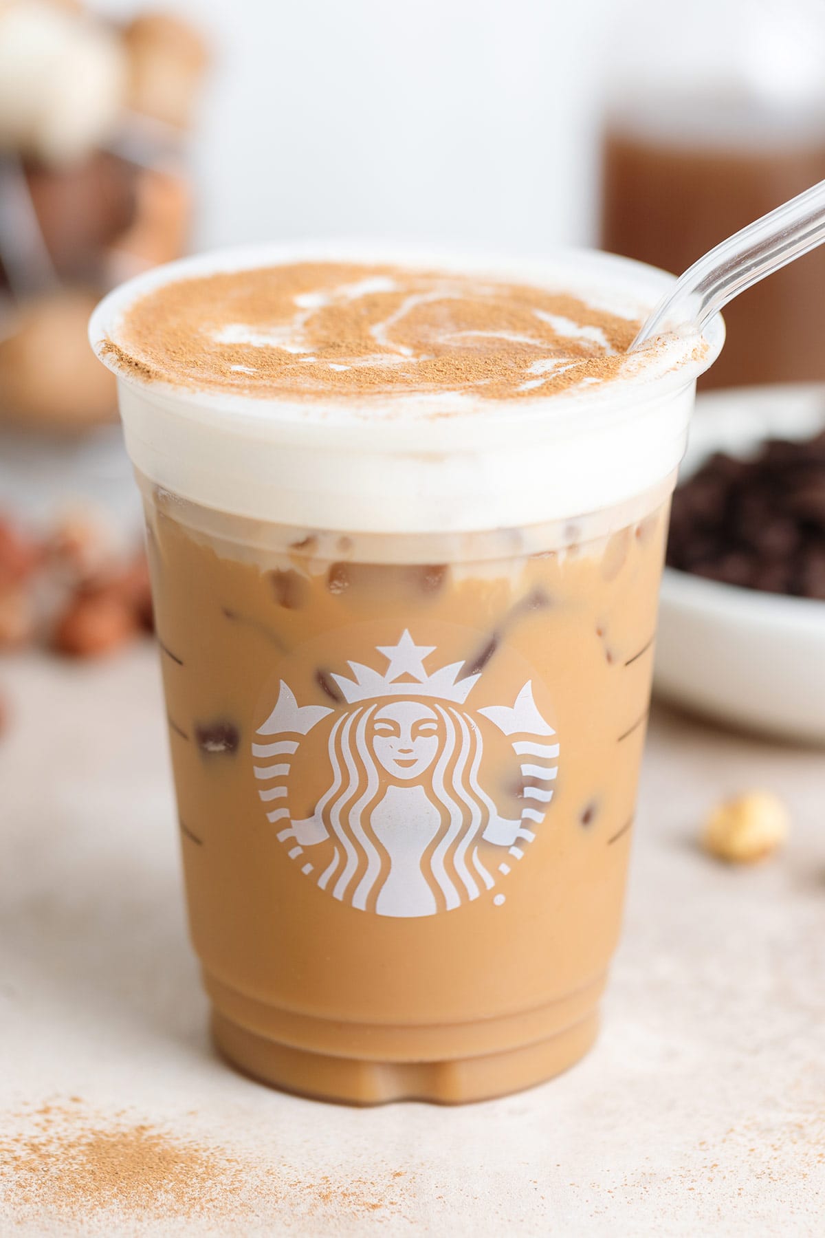 A plastic Starbucks cup with iced latte with frothy milk and a sprinkle of cinnamon with a glass straw on the right side of the cup.
