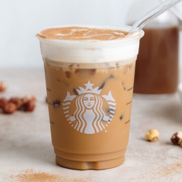 A plastic Starbucks cup with iced latte with frothy milk and a sprinkle of cinnamon with a glass straw on the right side of the cup.
