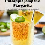 Bright yellow margarita in a short glass garnished with tajin, a wedge of pineapple, a slice of lime, and a slice of jalapeno with more fruits and drinks in the backround.