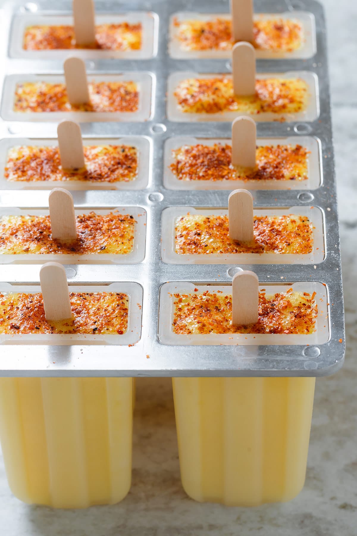 Bright yellow pineapple popsicles in popsicle molds garnished with tajin before freezing.