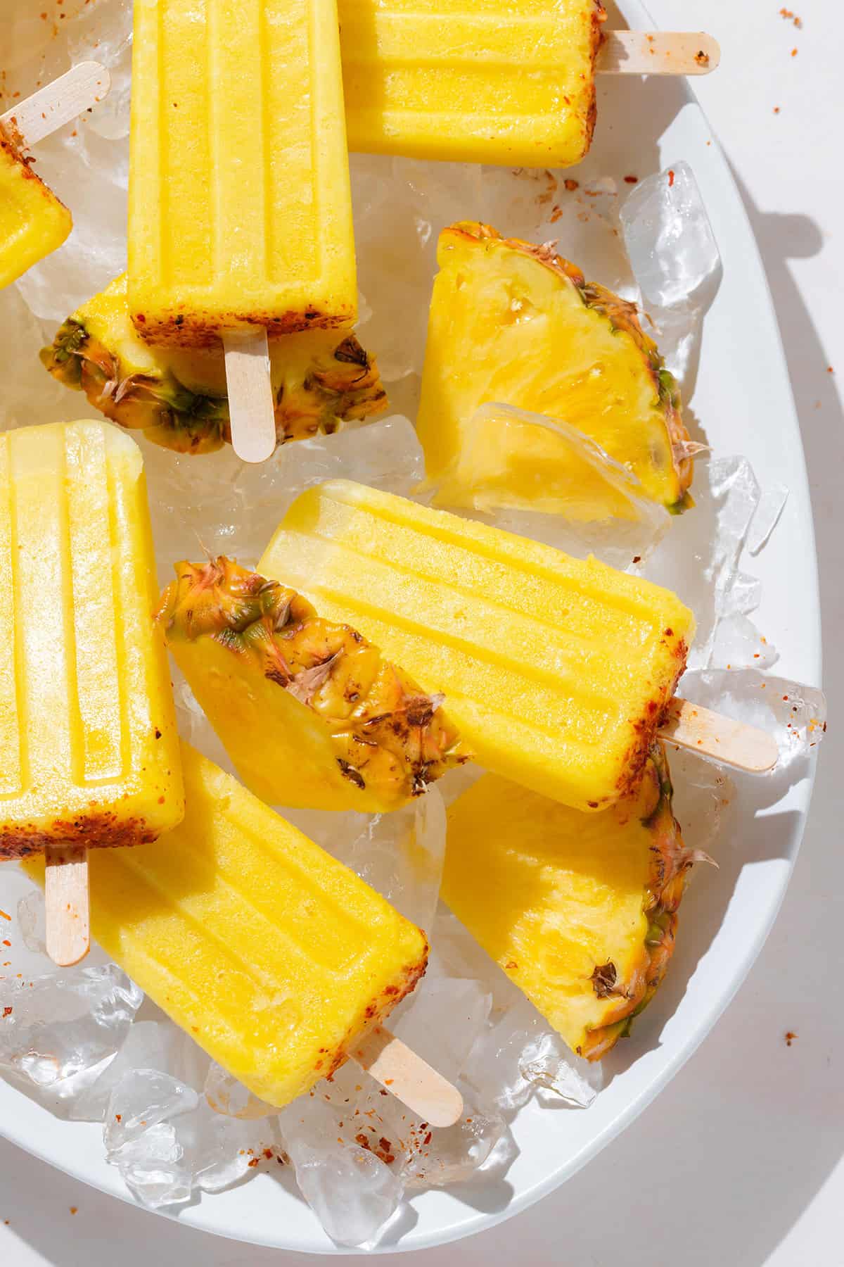 Pineapple popsicles with tajin on a large serving platter with ice and fresh pineapple slices.