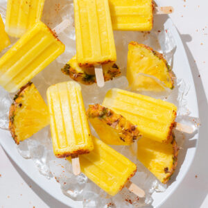 Pineapple popsicles with tajin on a large serving platter with ice and fresh pineapple slices.