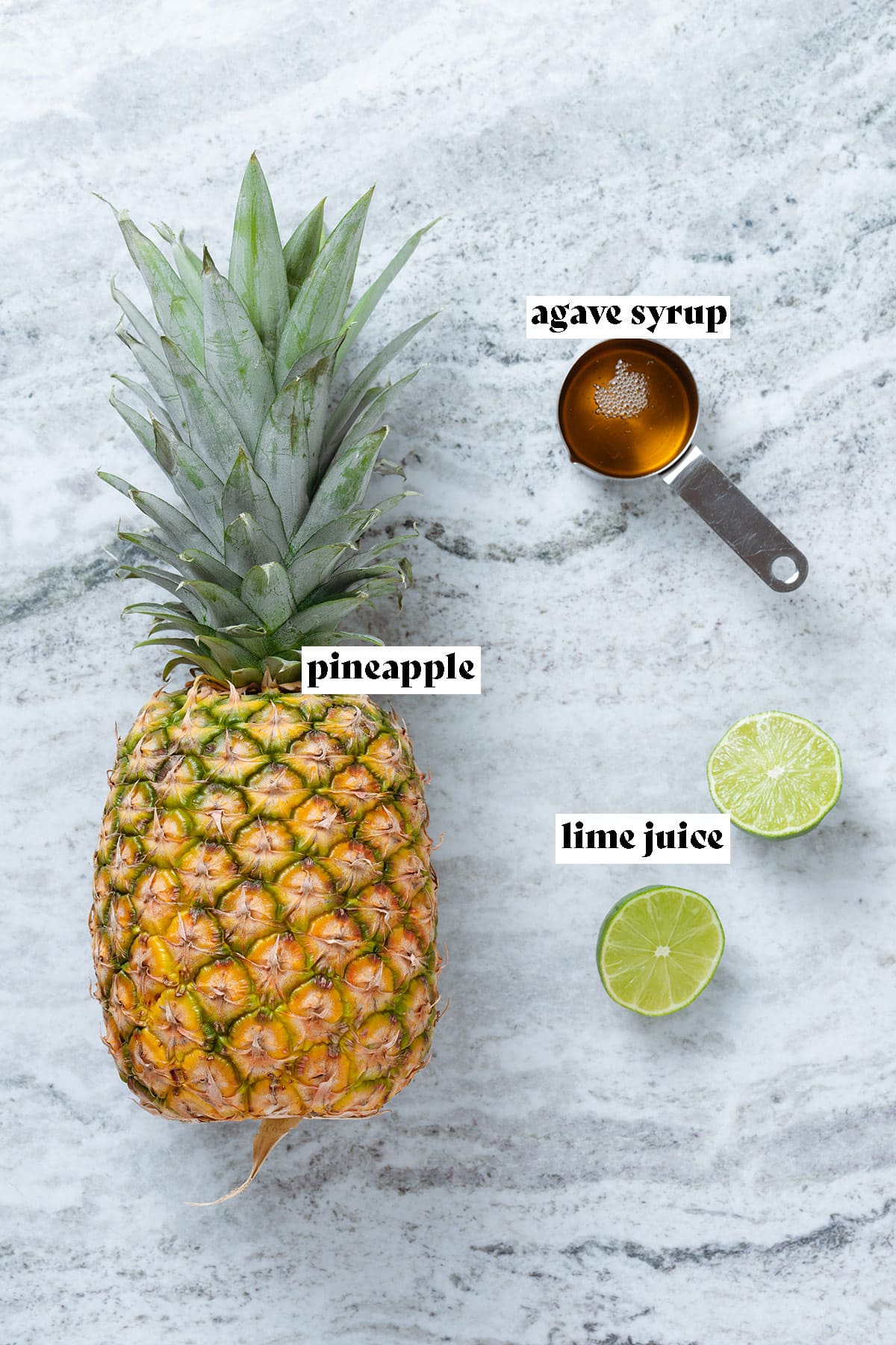 Pineapple, lime, and agave syrup laid out on a grey stone backround.