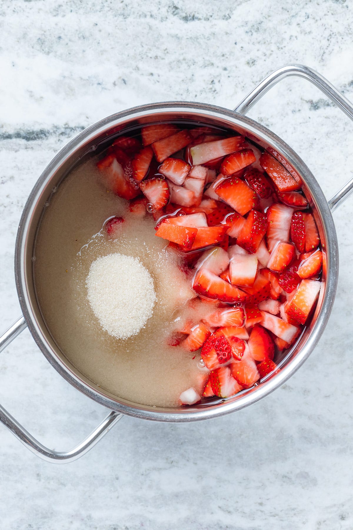 Fresh chopped strawberries with water and cane sugar in a small pot before cooking.
