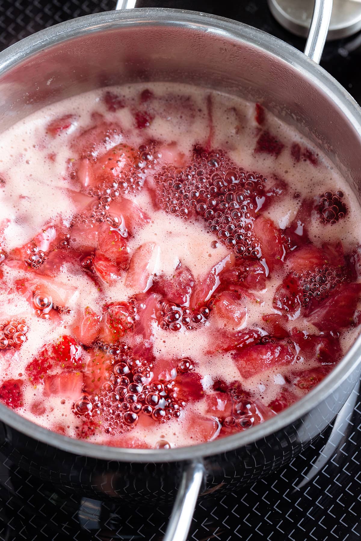 Chopped strawberries simmering with water and sugar on the stove.