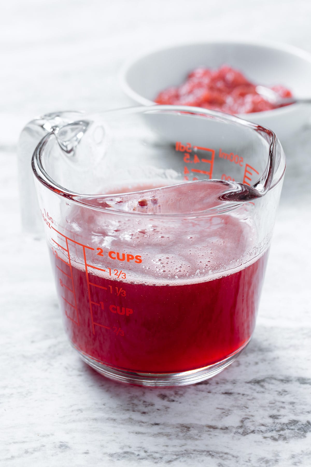 Strained strawberry syrup in a large glass measuring cup on a stone background.