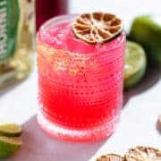 Bright pink margarita in a short glass garnished with a dehydrated lime slice.