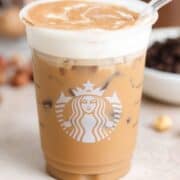 A plastic Starbucks cup with iced latte with frothy milk and a sprinkle of cinnamon with a glass straw on the right side of the cup.