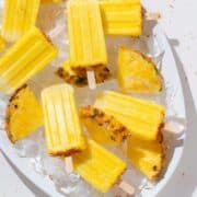 Pineapple popsicles with tajin on a large serving platter with ice and fresh pineapple slices.